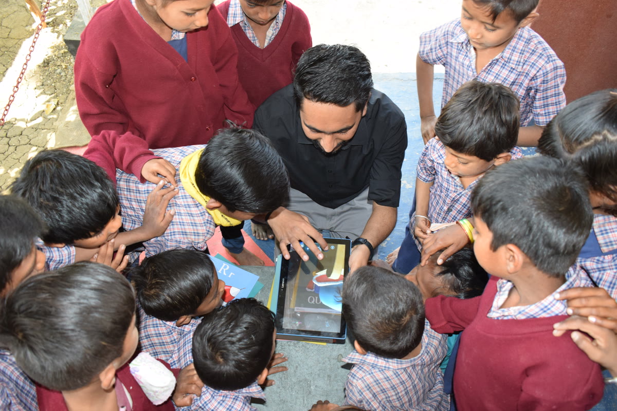 A circle of uniformed children leaning in to watch a tablet outdoors